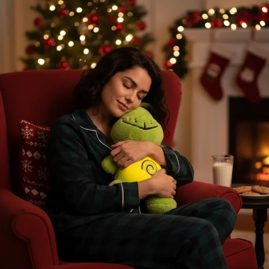 Woman in pajamas hugging plush toy by Christmas tree and fireplace with milk and cookies